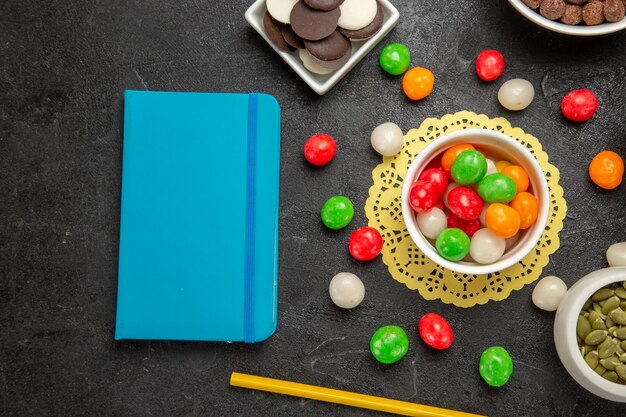 Vista superior de semillas de calabaza frescas con galletas y caramelos de colores sobre fondo gris oscuro, colores del arco iris, semillas de caramelo