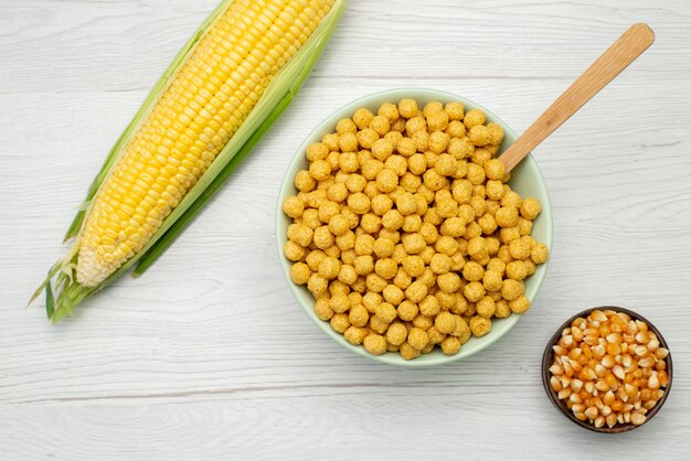 Vista superior de semillas de maíz de color amarillo con cereales dentro de la placa en blanco