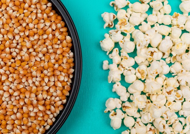 Vista superior de semillas de palomitas de maíz en una bandeja metálica negra a la izquierda y preparada a la derecha en una superficie azul horizontal