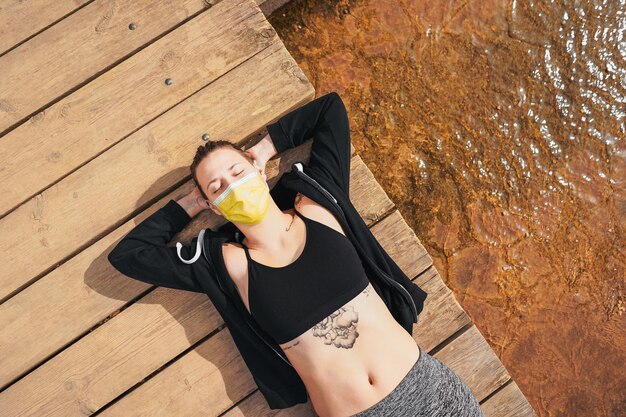 Vista superior de la sexy mujer española en una mascarilla con tatuajes descansando después del ejercicio en el parque