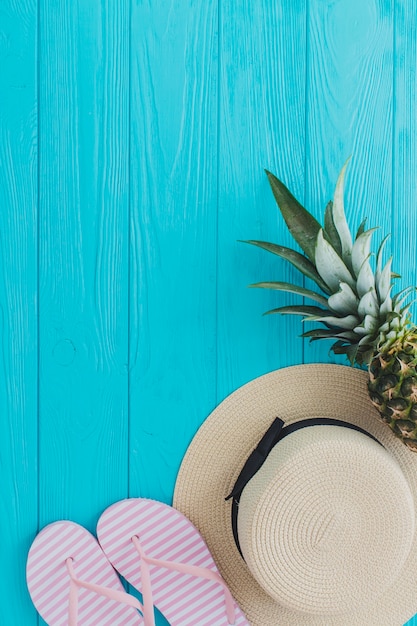 Foto gratuita vista superior de sombrero, piña y chanclas sobre superficie de madera azul