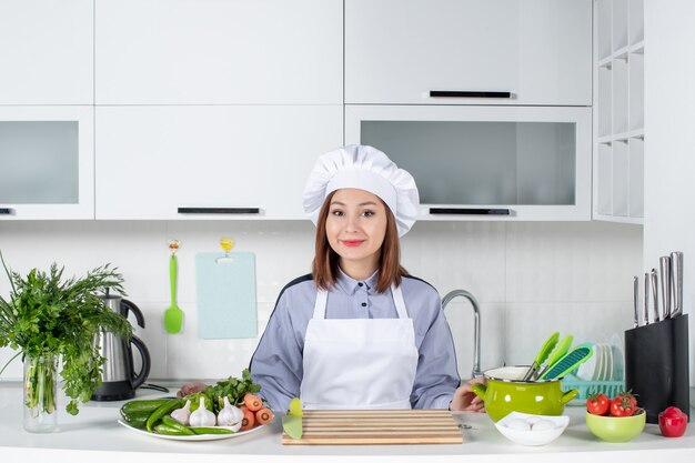 Vista superior de la sonriente chef femenina y verduras frescas en la cocina blanca