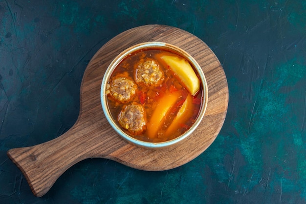 Vista superior de sopa de albóndigas con patatas dentro de la ronda sobre la superficie azul oscuro