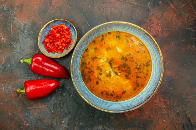 Vista superior de la sopa de arroz en tazón azul pimientos picados en un tazón pimientos frescos en la mesa de color rojo oscuro