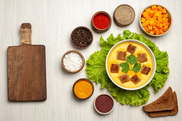 Vista superior de la sopa de calabaza con pequeños bizcochos de pan y condimentos en blanco