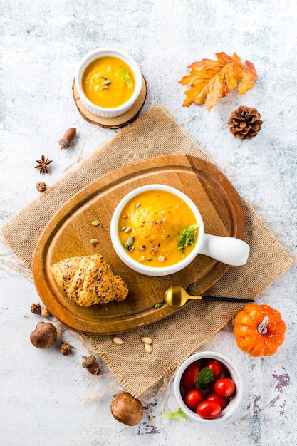 Vista superior de sopa de calabaza en tablero de madera rodeado de verduras de otoño