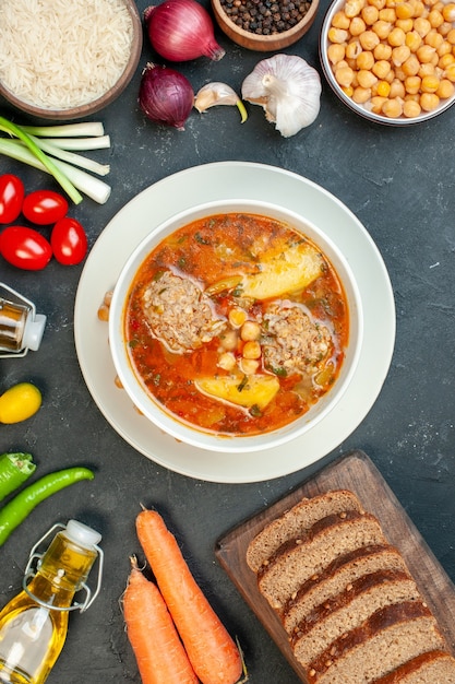 Vista superior de la sopa de carne con hogazas de pan y condimentos sobre fondo oscuro