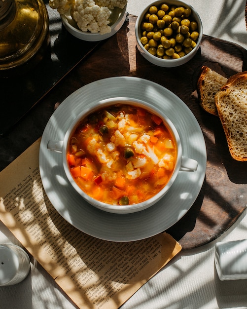 Vista superior de sopa con coliflor zanahoria y papas sobre una plancha de madera