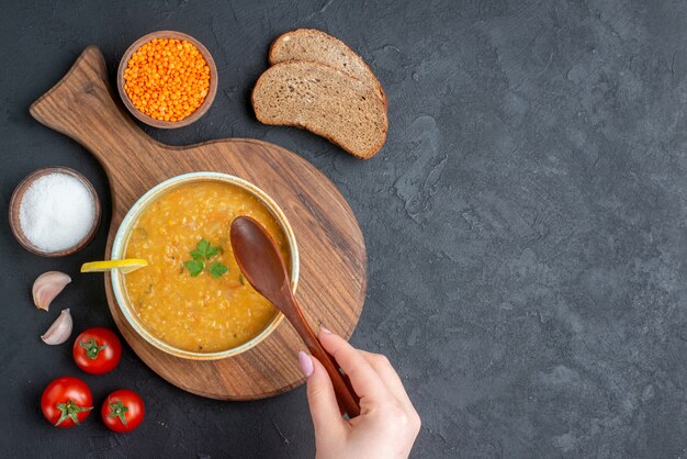 Vista superior de la sopa de lentejas con tomates salados y panes de pan oscuro sobre una superficie oscura