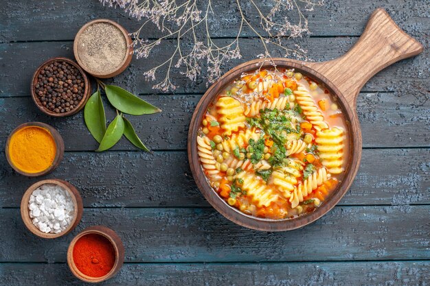 Vista superior de sopa de pasta en espiral con diferentes condimentos en la cocina de plato de pasta italiana de color azul oscuro sopa de escritorio