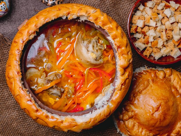 Vista superior sopa de pollo en una jarra de barro con galletas y una tapa de masa