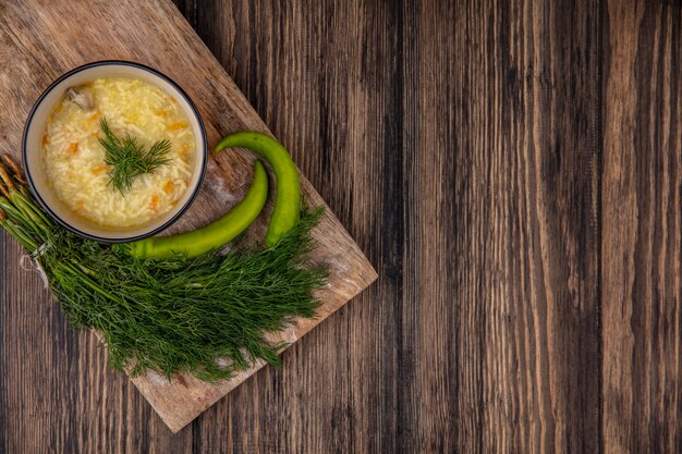 Foto gratuita vista superior de la sopa de pollo orzo en un tazón y pimientos con eneldo en la tabla de cortar sobre fondo de madera con espacio de copia