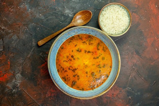 Vista superior de la sopa en el tazón de fuente azul tazón de fuente de arroz cuchara de madera en la mesa de color rojo oscuro