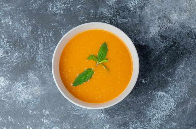 Vista superior de la sopa de tomate casera fresca en un tazón blanco sobre la mesa gris.