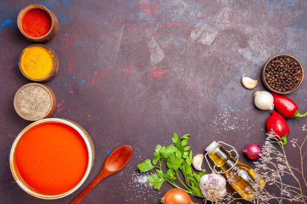 Vista superior de la sopa de tomate cocinada con tomates frescos con diferentes condimentos en negro