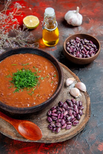 Vista superior de la sopa de tomate, frijoles, ajo sobre tabla de cortar de madera y botella de aceite en la mesa de mezcla de colores