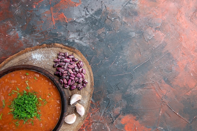 Vista superior de la sopa de tomate, frijoles, ajo sobre tabla de cortar de madera sobre fondo de color de mezcla
