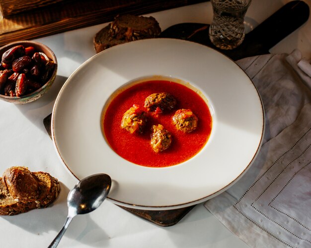 Vista superior sopa de tomate con rollitos de carne junto con rebanadas de pan en la superficie blanca