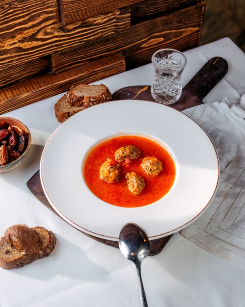 Vista superior sopa de tomate con rollos de carne en el interior junto con rebanadas de pan en el escritorio blanco