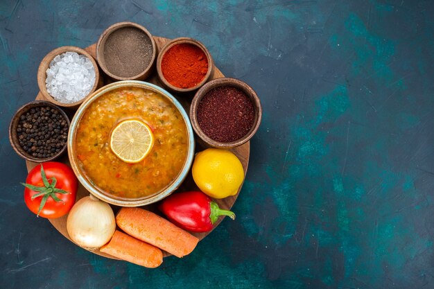 Vista superior de sopa de verduras con limón junto con condimentos y verduras frescas en una superficie azul oscuro