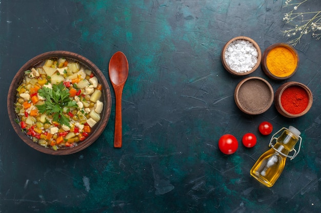 Vista superior de sopa de verduras con verduras junto con condimentos y aceite de oliva sobre fondo oscuro