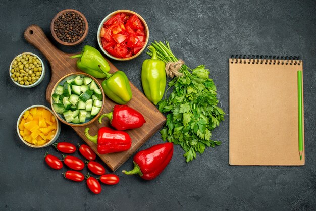 Vista superior del soporte para platos con verduras encima y cerca de él y el bloc de notas en el costado sobre un fondo grisáceo oscuro