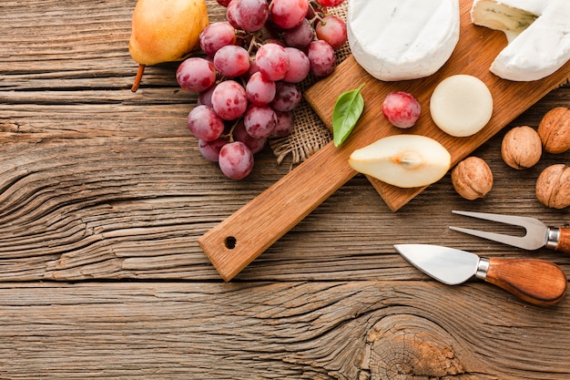 Vista superior surtido de quesos gourmet en tabla de cortar de madera con uvas y utensilios