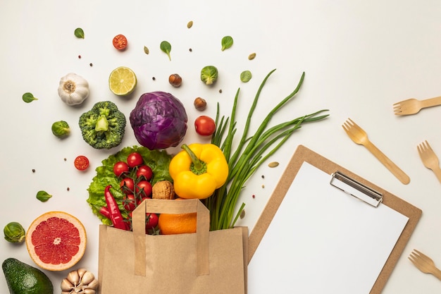 Vista superior del surtido de verduras en bolsa de papel con portapapeles