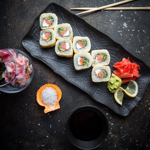Vista superior de sushi con jengibre encurtido y wasabi y salsa de soja y palillos en plato oscuro