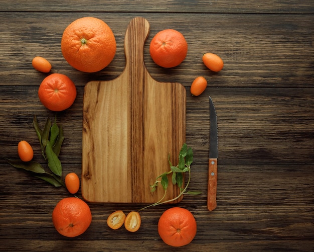 Vista superior de la tabla de cortar con cuchillo kumquat naranja mandarina alrededor sobre fondo de madera