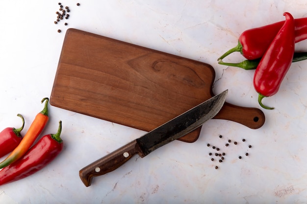 Vista superior de la tabla de cortar con cuchillo y pimientos y especias de pimienta sobre fondo blanco.