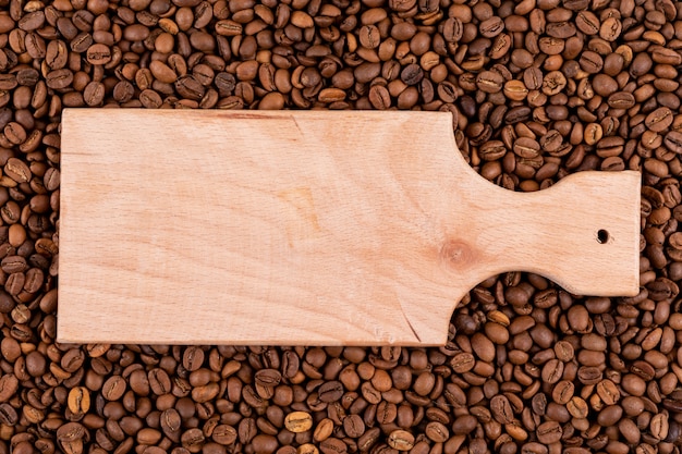 Vista superior tabla de cortar de madera en la superficie de granos de café