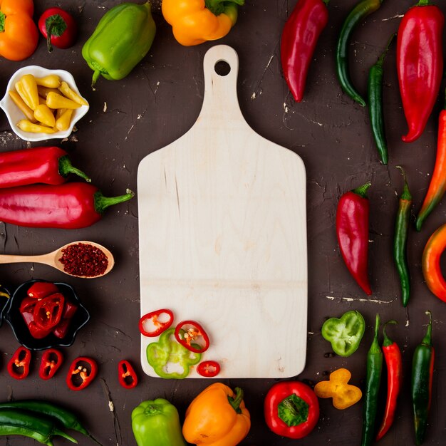 Vista superior de la tabla de cortar con pimientos, pimienta salada sobre fondo marrón