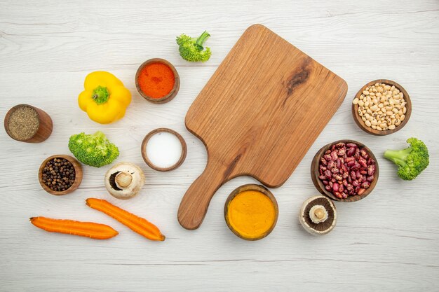 Vista superior de la tabla de cortar setas, frijoles de brócoli, cuencos, diferentes especias, zanahorias cortadas en la mesa