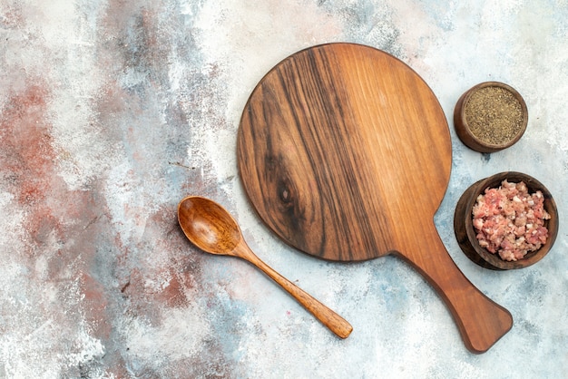 Foto gratuita vista superior de una tabla de cortar tazones con cuchara de madera de carne de pimienta en lugar libre de fondo desnudo