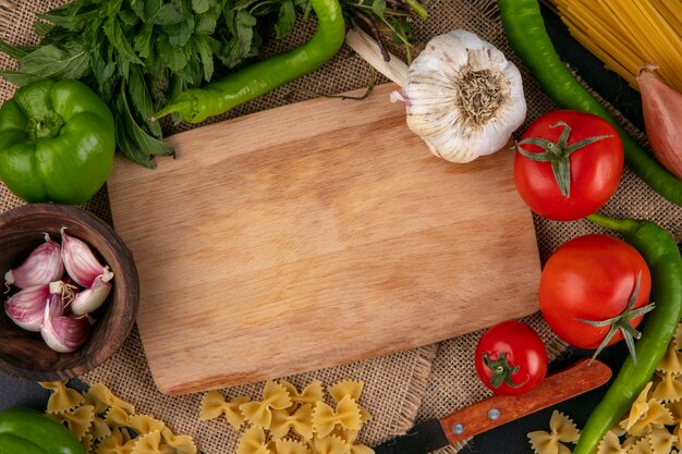 Vista superior de la tabla de cortar con tomates campana de ajo y pimientos picantes y cebollas con menta en una servilleta beige