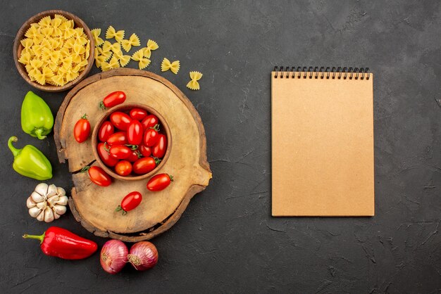 Vista superior de la tabla de cortar de verduras apetitosas con un plato de pasta de tomates y ajo de cebolla de pimiento junto al cuaderno de crema