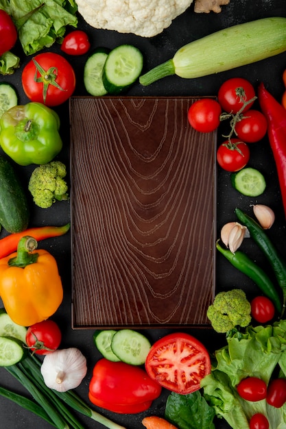 Vista superior de la tabla de cortar con verduras como pimiento, tomate, calabacín, ajo y otros alrededor sobre fondo negro