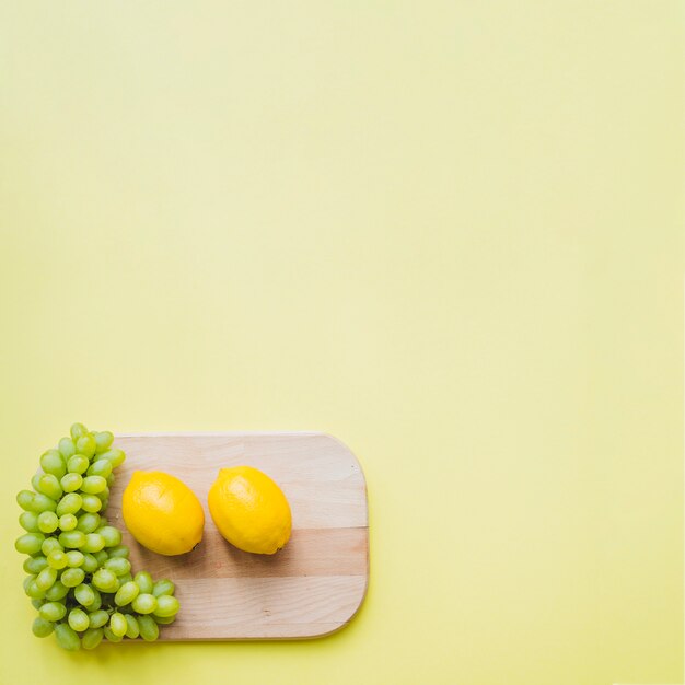 Vista superior de table de cortar con limones y racimo de uvas