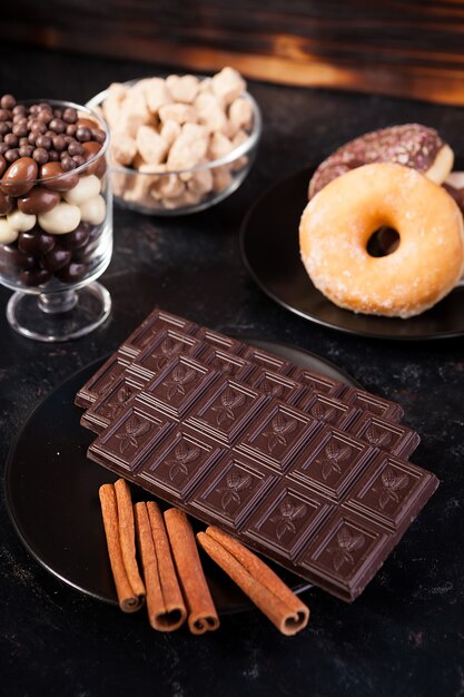 Vista superior de tabletas de chocolate, donas, azúcar morena con maní en chocolate y granos de café sobre fondo oscuro de madera vintage