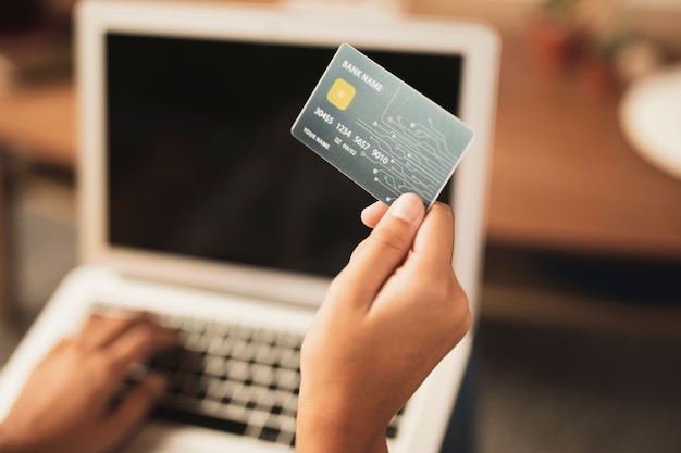 Vista superior de la tarjeta de crédito en la mano con portátil borrosa en el fondo