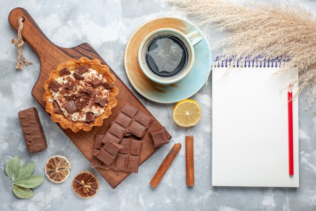 Vista superior de la tarta de crema con barras de chocolate Bloc de notas y té en la mesa de luz pastel dulce azúcar crema chocolate