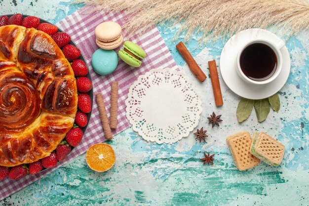 Vista superior de tarta de fresa con galletas macarons franceses y taza de té en la superficie azul claro