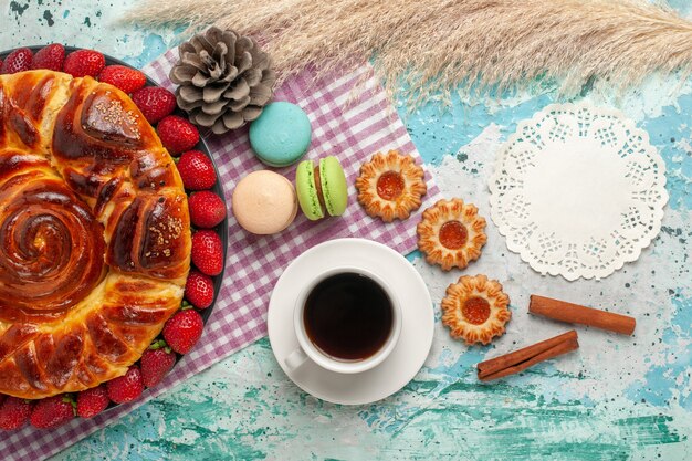 Vista superior de tarta de fresa con galletas macarons franceses y taza de té en superficie azul