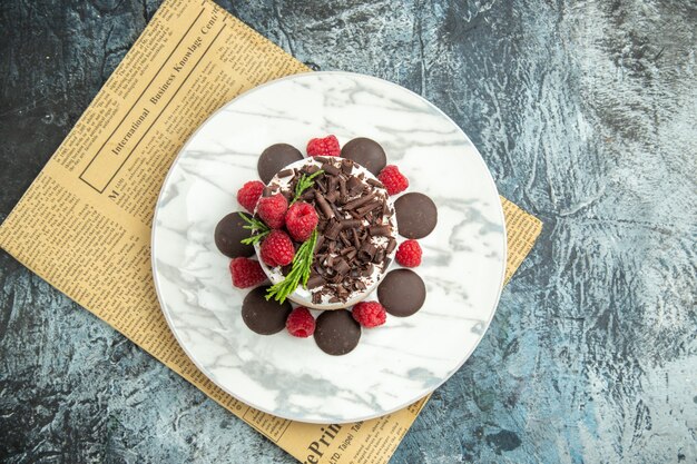 Vista superior de tarta de queso con chocolate y frambuesas en el periódico plateon ovalado blanco en el espacio libre de la superficie gris