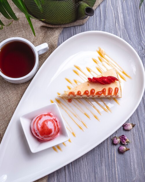 Vista superior tarta de queso de postre con helado de fresa y en rodajas ‹fresas con una taza de té sobre la mesa