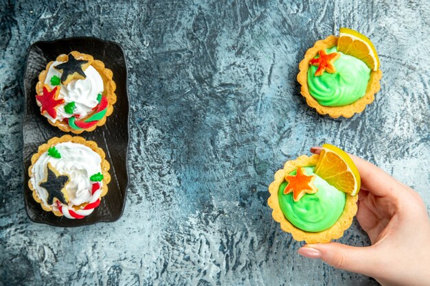 Vista superior de tartas de Navidad en placa negra tarta pequeña en mano femenina en espacio libre de mesa gris