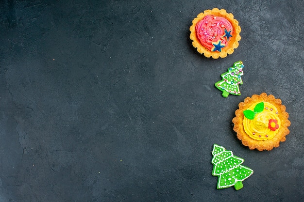 Vista superior de tartas pequeñas galletas de árbol de Navidad en lugar libre de mesa oscura