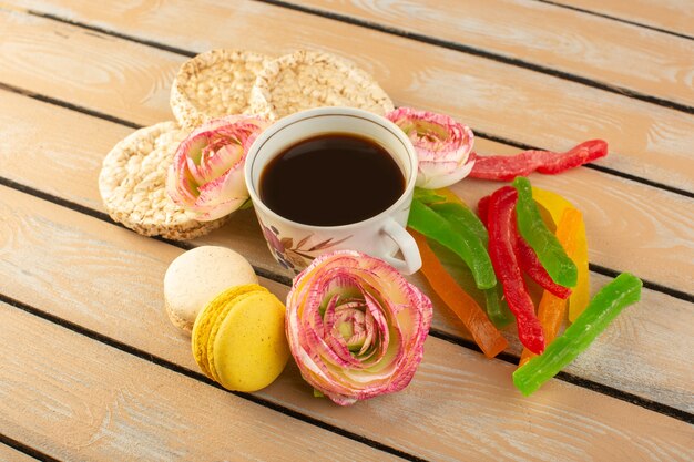 Vista superior de una taza de café caliente y fuerte con flores de macarons franceses y mermelada en el escritorio rústico de color crema beber café foto fuerte