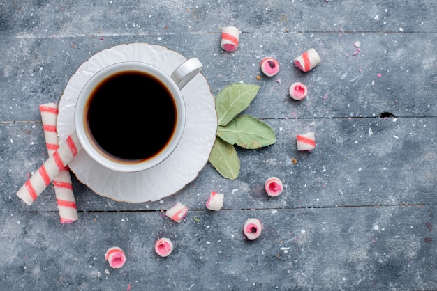 Vista superior de la taza de café caliente y fuerte junto con caramelos de palo rosa en gris, bebida dulce de caramelo de café